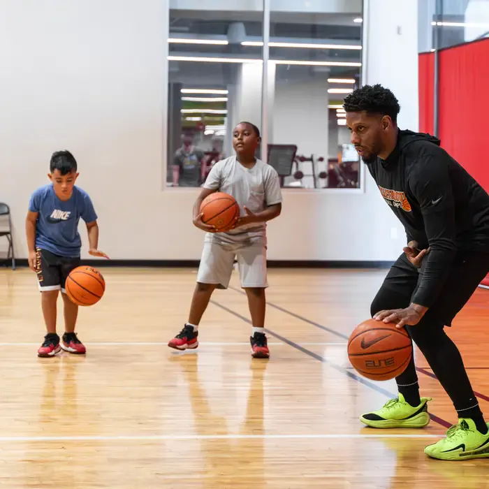 Coach modeling a dribbling drill while two young players follow along
