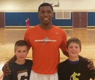 Basketball coach poses with two young children on indoor court during camp