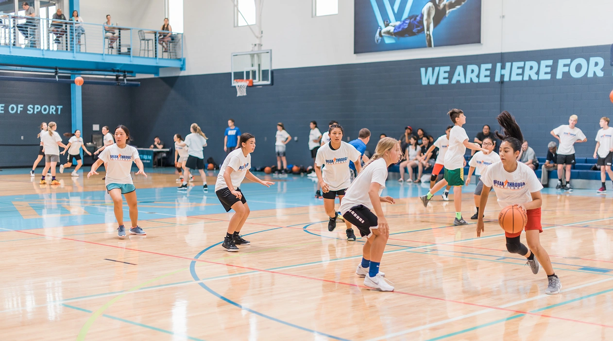 Young boys playing basketball in a gym, practicing dribbling and defense during a training session while a coach observe in the background