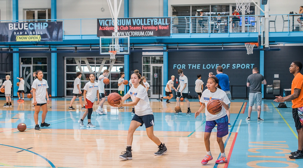 Young boys playing basketball in a gym, practicing dribbling and defense during a training session while a coach observe in the background