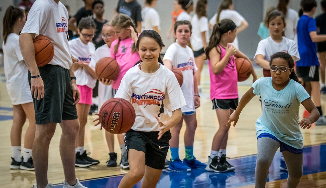 Focused young girl practicing basketball dribbling drills in a gym